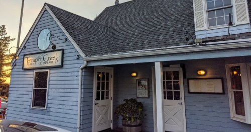 Exterior of Terrance Creek restaurant, featuring a blue wooden facade, two doors, and a sign above the entrance.