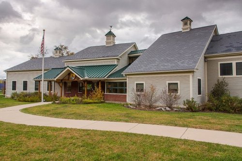 A two-story building with a green roof, flagpole, and landscaped lawn under a cloudy sky.