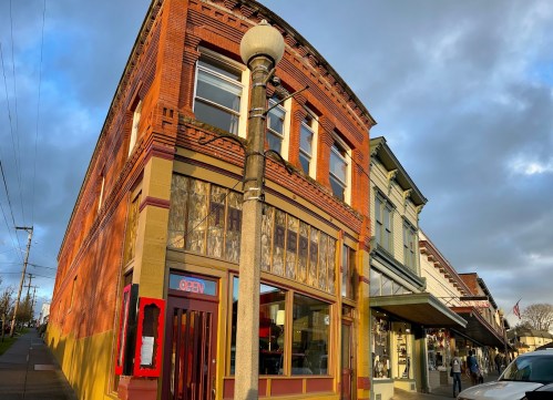 Historic brick building with a colorful facade, featuring a shop window and an "OPEN" sign, under a cloudy sky.