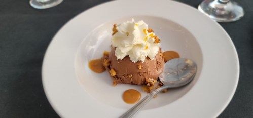 A dessert featuring chocolate mousse topped with whipped cream and crushed nuts, served on a white plate.
