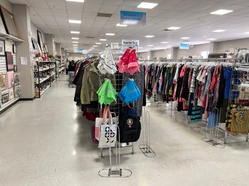 A spacious thrift store aisle with racks of women's clothing and accessories on display.