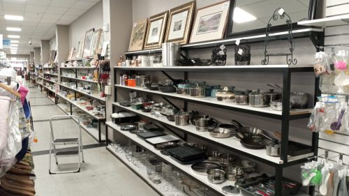 A store aisle with shelves displaying various cookware, utensils, and framed art on the walls.