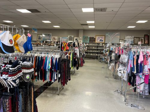 A spacious thrift store aisle filled with clothing racks and shelves displaying various items for sale.