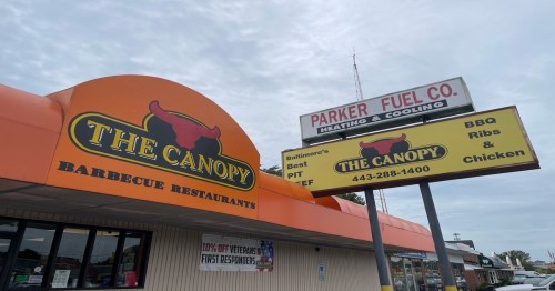 Signage for The Canopy Barbecue Restaurant featuring BBQ ribs and chicken, with a nearby fuel company sign.