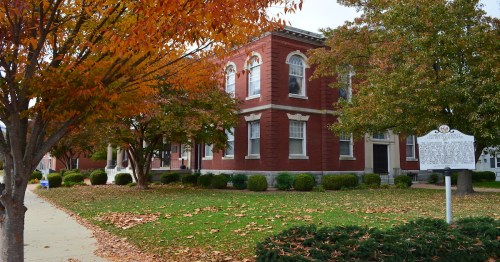 Historic red brick building surrounded by autumn foliage and a grassy area with fallen leaves.