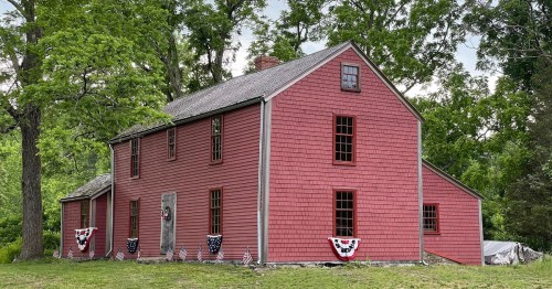 A red wooden house surrounded by trees, decorated with patriotic bunting and flags.