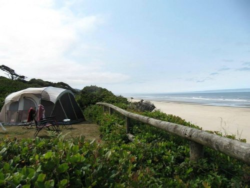 A tent set up on a grassy area overlooking a sandy beach and ocean under a cloudy sky.