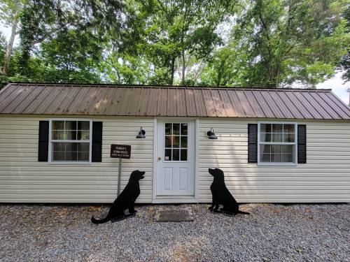 A small, light-colored cabin with a metal roof, flanked by two black dog silhouettes on either side of the door.