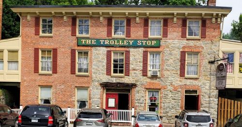 A brick building with a stone facade, featuring the sign "The Trolley Stop" and parked cars in front.