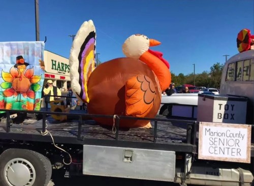 A large inflatable turkey on a truck, decorated for a parade, with colorful banners and a sign for the Marion County Senior Center.