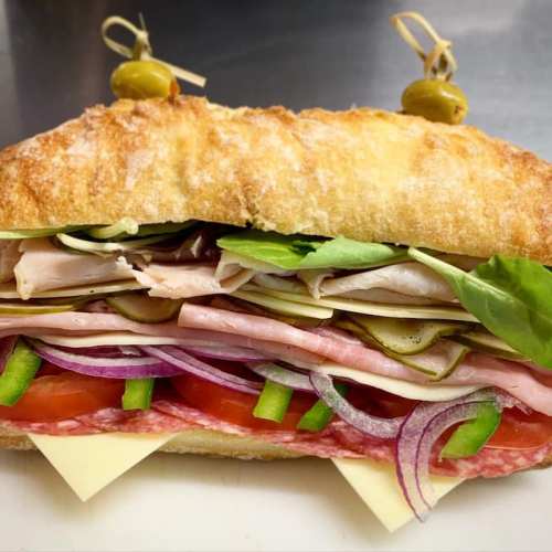 A close-up of a sandwich filled with layers of meats, cheese, lettuce, tomatoes, and onions, served on a crusty roll.