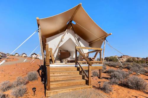 A glamping tent with a wooden deck set in a desert landscape under a clear blue sky.