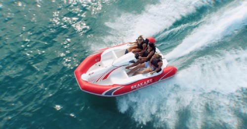A group of four people enjoying a ride on a small speedboat, creating waves in the turquoise water.