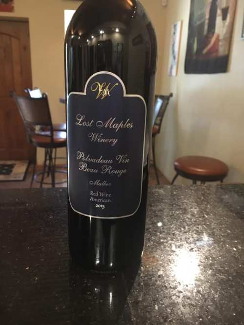 A bottle of Lost Maples Winery 2015 Polka Dot Vin Beau Rouge red wine on a dark countertop.