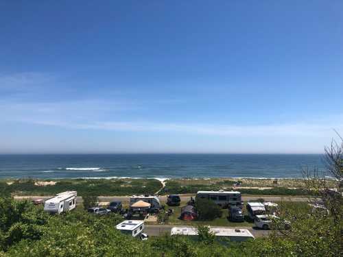 A scenic view of a beach with RVs parked nearby, under a clear blue sky and calm ocean waves.