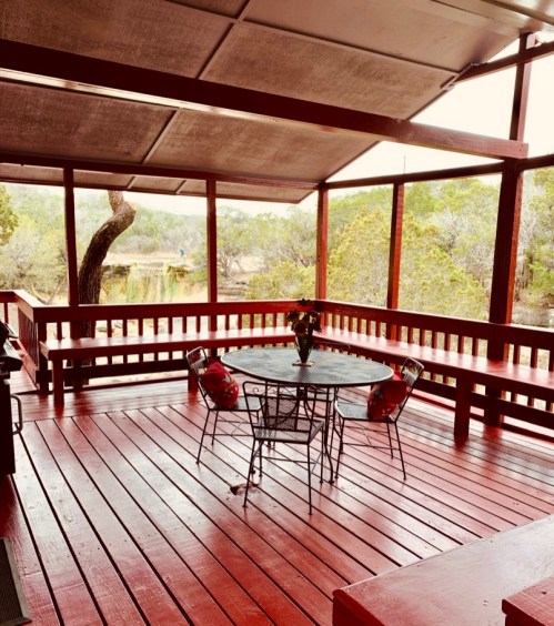 A cozy outdoor patio with a round table and chairs, surrounded by greenery and a peaceful view.