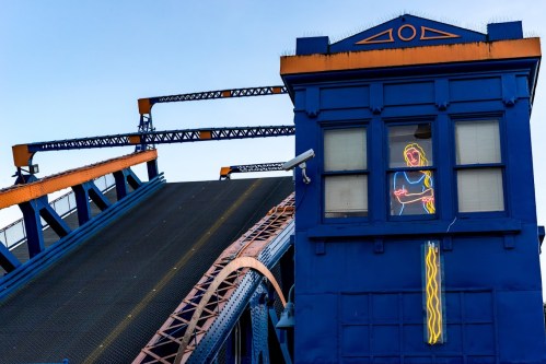 A colorful bridge control tower with a neon figure in the window, set against a clear blue sky.