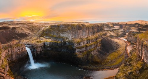 A stunning sunset over a canyon with a waterfall cascading into a serene pool below, surrounded by rugged cliffs.