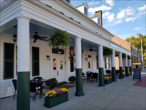 A charming restaurant exterior with white columns, potted plants, and outdoor seating on a sunny day.