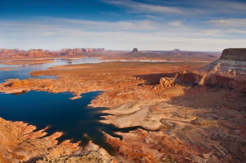 A vast desert landscape with a winding river, rocky formations, and a clear blue sky in the background.