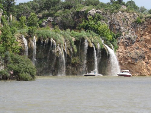 A scenic view of a waterfall cascading over rocky cliffs, with two boats on the calm water below.