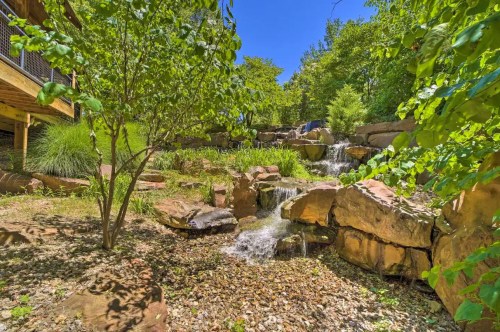 A serene landscape featuring a small waterfall surrounded by rocks and lush greenery under a clear blue sky.