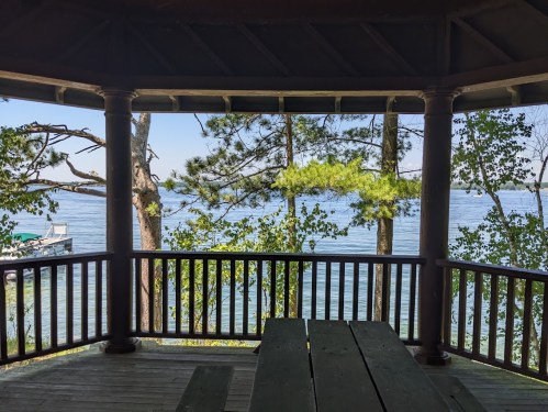 View from a gazebo overlooking a calm lake, framed by trees and a wooden railing.