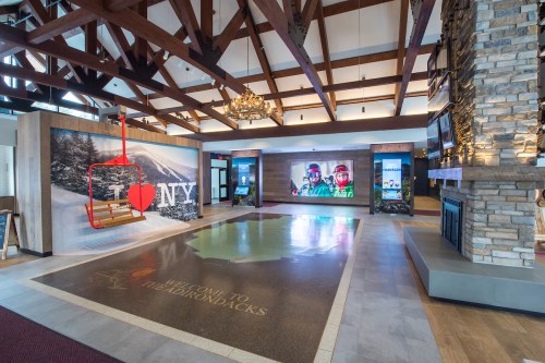 Interior of a lodge with wooden beams, a ski lift display, and a welcome sign for the Adirondacks.