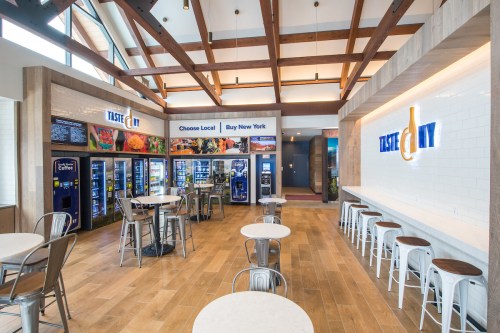 A modern food hall with vending machines, tables, and a bright, open design featuring wooden beams and a welcoming atmosphere.