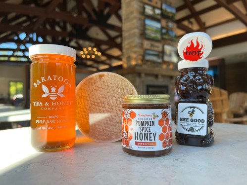 Three jars of honey: pure raw honey, pumpkin spice honey, and a bear-shaped honey bottle, set on a table in a cozy interior.