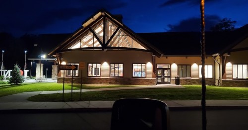 A well-lit building with a large glass entrance, surrounded by green grass, at night under a blue sky.