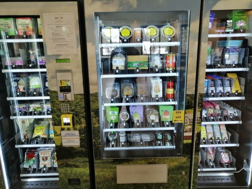 A vending machine filled with various snacks and drinks, set against a green landscape background.