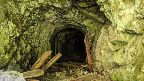 A dark, rocky mine entrance with wooden beams and debris scattered on the ground.