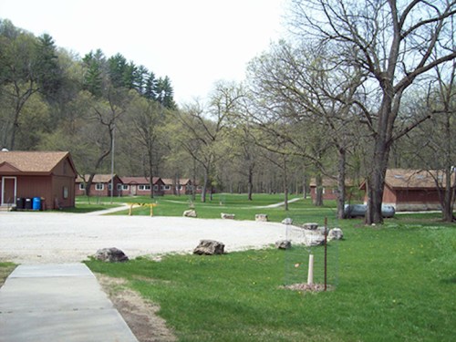 A peaceful outdoor scene featuring cabins, green grass, and trees in a natural setting.