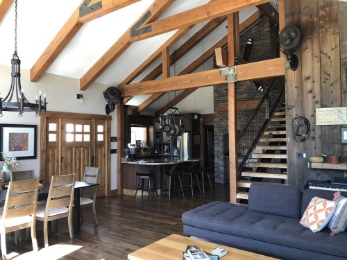 Cozy interior of a modern cabin featuring wooden beams, a staircase, and a living area with a sofa and dining table.