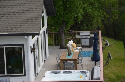 A spacious deck with outdoor furniture, a grill, and a hot tub, surrounded by greenery and trees.