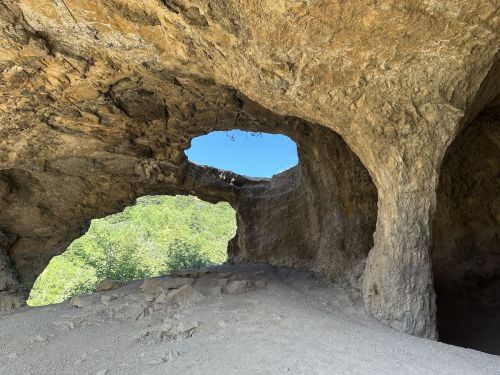 A rocky cave with two openings, revealing a bright blue sky and greenery outside.