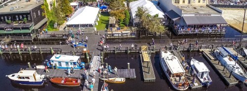 Aerial view of a waterfront festival with tents, boats, and people along the docks.