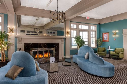Cozy lounge with blue curved sofas, a fireplace, and green chairs, featuring a stylish, modern decor.
