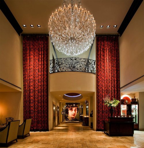 Elegant hotel lobby featuring a grand chandelier, red drapes, and a large portrait on the wall.
