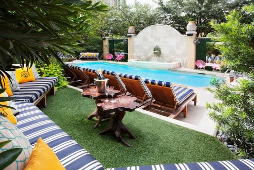A serene poolside scene with lounge chairs, a small table, and lush greenery surrounding a sparkling blue pool.