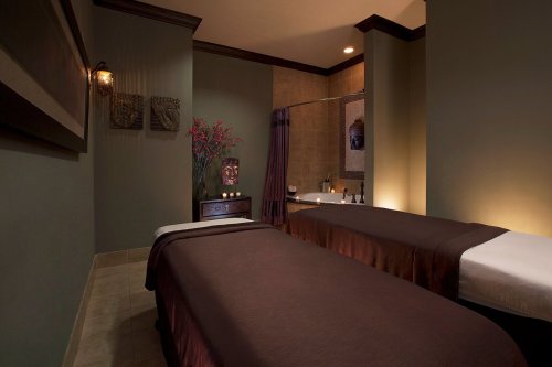 A serene spa room with two massage tables, soft lighting, and decorative elements creating a calming atmosphere.