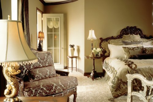 Elegant bedroom featuring a plush bed, ornate furniture, and soft lighting from lamps. Warm, inviting decor.