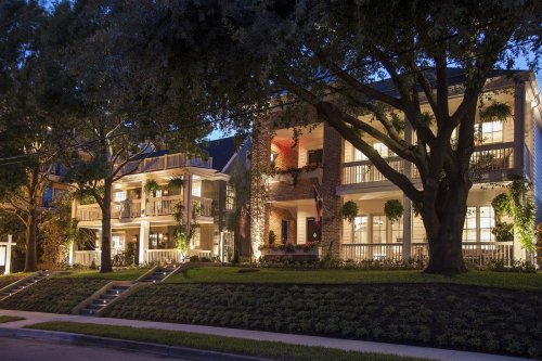A row of beautifully lit houses at dusk, surrounded by lush greenery and large trees.