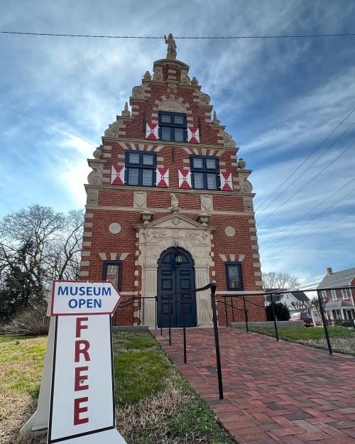 Historic brick museum building with decorative facade, flags, and a sign indicating it's open and free to visit.