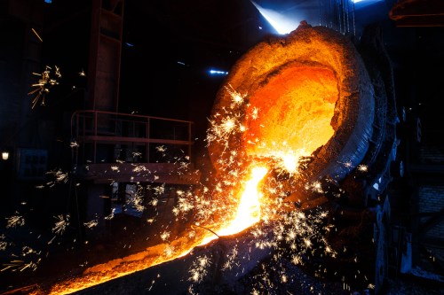 Molten metal pours from a furnace, creating bright sparks in a dark industrial setting.