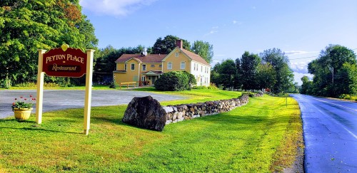 A yellow restaurant building with a sign, surrounded by greenery and a stone wall, alongside a quiet road.