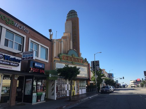 Art Deco-style Crest Theatre marquee beside storefronts on a sunny street, with clear blue skies above.