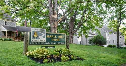 Sign for Maple Hill Farm, featuring hiking trails and gardens, surrounded by trees and greenery.