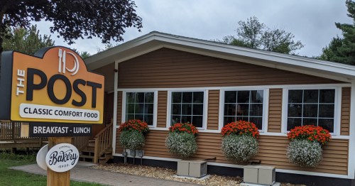 A cozy restaurant exterior with a sign reading "The Post" and flower planters, promoting classic comfort food.